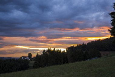 Evin önünde bir dramatik akşam gökyüzü günbatımı için ağaçların arasındaki kara orman