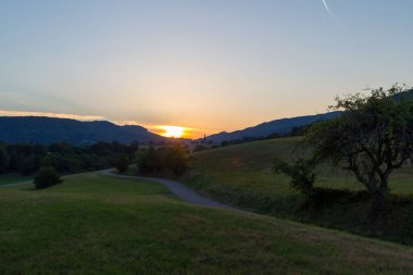 Gün batımında Kara Orman 'daki çayırlar arasında küçük bir köy yolu.