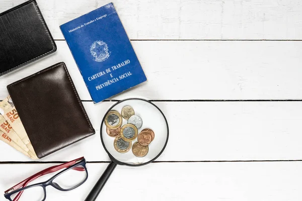 work permit, wallet,  Brazilian money, Brazilian coins, magnifying glasses, glasses, leather notepad, white background, space for text, pinus background, objects on the left, top view