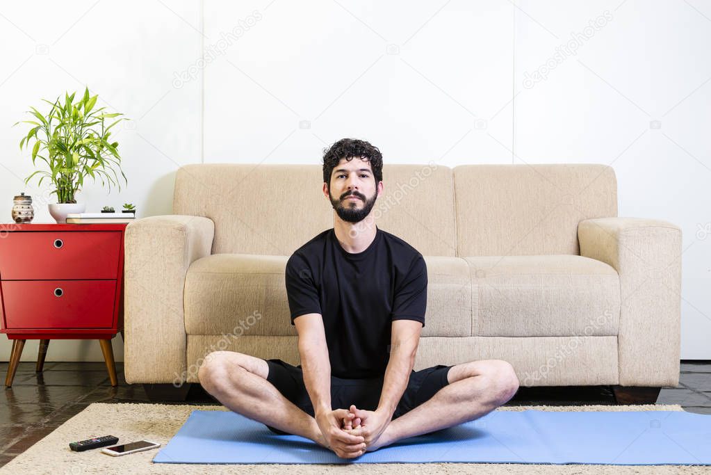 Beautiful caucasian bearded man in black clothes on blue yogamat doing gracious posture with open eyes