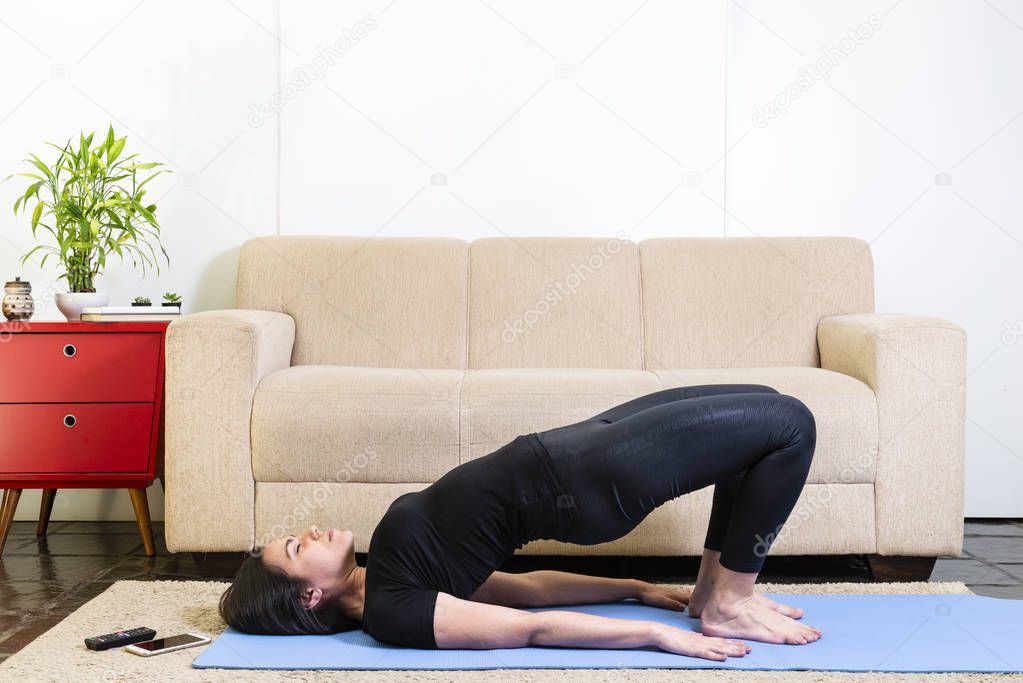 Beautiful caucasian brunette woman in black clothes on blue yogamat doing bridge pose