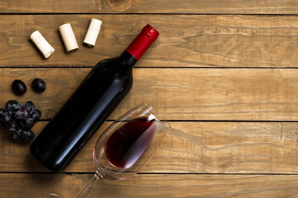 Bottle of wine and glass corks and grapes on wooden background. Top view with copy space.