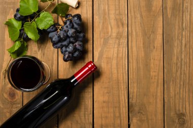 Şişe ve cam şarap ile demet üzüm ve asma ahşap arka plan üzerinde bırakır. Kopya alanı ile üstten görünüm.