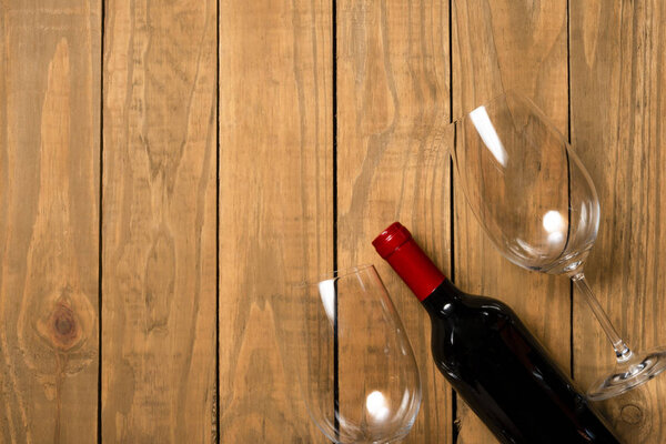 Bottle of wine and glass cups on wooden background. Top view with copy space.