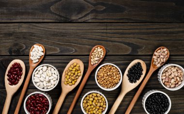 Tahta kaşıklar içinde fasulye çeşitliliği. Siyah ahşap arka plan.