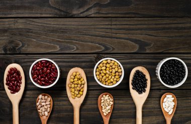 Tahta kaşıklar içinde fasulye çeşitliliği. Siyah ahşap arka plan.