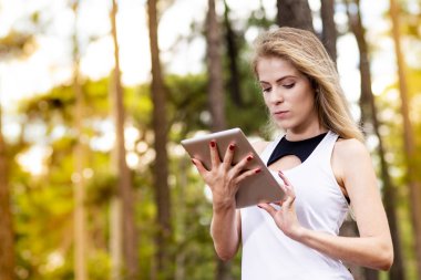 Tablet kullanarak güzel modeli. Arka plan günbatımı ışığı ile bulanık orman