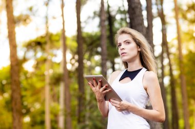 Tablet kullanarak güzel modeli. Arka plan günbatımı ışığı ile bulanık orman