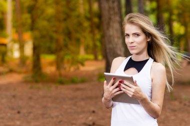 Kuru üzerinde oturan sarışın model okuma onun tablet üzerinde sopa. Gün batımında bulanık arka plan