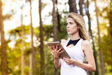 Tablet kullanarak güzel modeli. Arka plan günbatımı ışığı ile bulanık orman