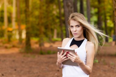 Kuru üzerinde oturan sarışın model okuma onun tablet üzerinde sopa. Gün batımında bulanık arka plan