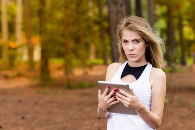 Kuru üzerinde oturan sarışın model okuma onun tablet üzerinde sopa. Gün batımında bulanık arka plan