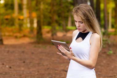 Kuru üzerinde oturan sarışın model okuma onun tablet üzerinde sopa. Gün batımında bulanık arka plan