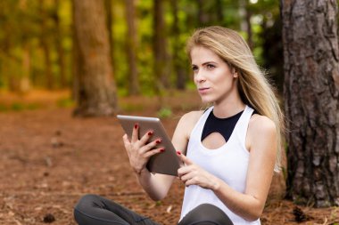 Kuru üzerinde oturan sarışın model okuma onun tablet üzerinde sopa. Gün batımında bulanık arka plan