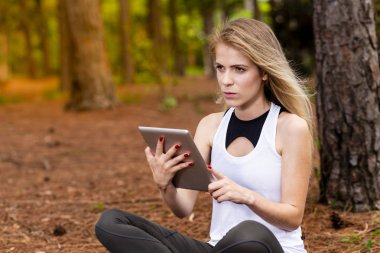 Kuru üzerinde oturan sarışın model okuma onun tablet üzerinde sopa. Gün batımında bulanık arka plan