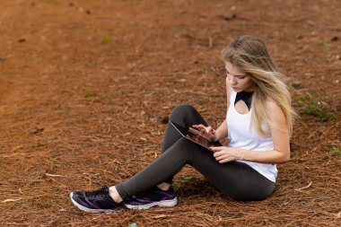 Kuru üzerinde oturan sarışın model okuma onun tablet üzerinde sopa. Gün batımında bulanık arka plan