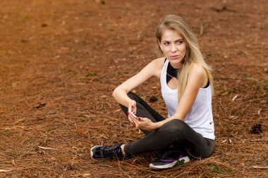 Kurutulmuş çam üzerinde oturan güzel sarışın model cep telefonu kullanarak ve müzik bırakır