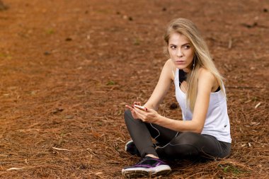 Kurutulmuş çam üzerinde oturan güzel sarışın model cep telefonu kullanarak ve müzik bırakır