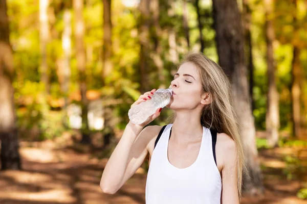 Güzel sarışın model spor giysileri ile şişe su ile. Gün batımında bulanık orman arka plan