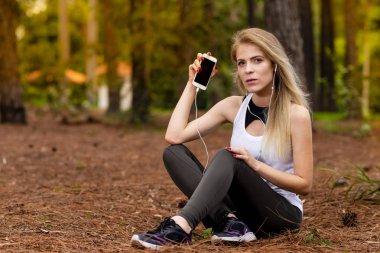 Pines ortasında güzel sarışın model cep telefonu ile kulaklık kullanarak oturma. Müzik