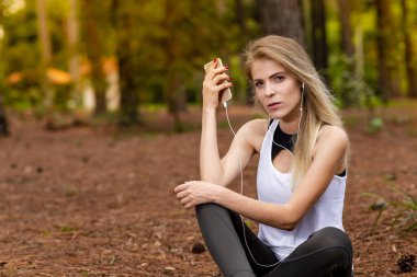 Pines ortasında güzel sarışın model cep telefonu ile kulaklık kullanarak oturma. Müzik