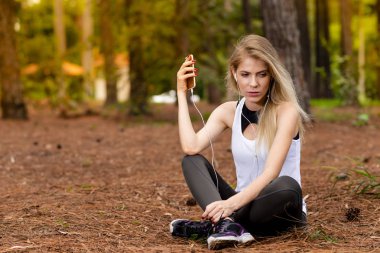 Pines ortasında güzel sarışın model cep telefonu ile kulaklık kullanarak oturma. Müzik