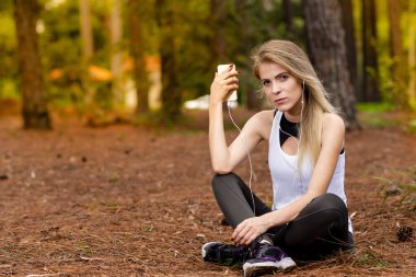 Pines ortasında güzel sarışın model cep telefonu ile kulaklık kullanarak oturma. Müzik