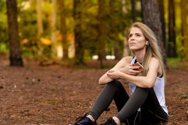 Pines ortasında güzel sarışın model cep telefonu ile kulaklık kullanarak oturma. Müzik
