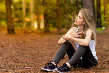 Pines ortasında güzel sarışın model cep telefonu ile kulaklık kullanarak oturma. Müzik
