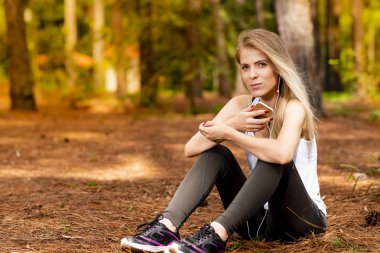 Pines ortasında güzel sarışın model cep telefonu ile kulaklık kullanarak oturma. Müzik