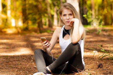 Pines ortasında güzel sarışın model cep telefonu ile kulaklık kullanarak oturma. Müzik