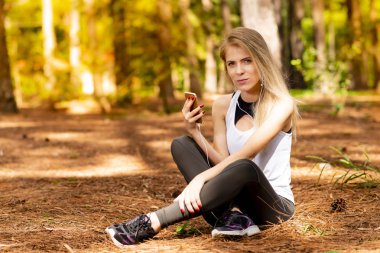 Pines ortasında güzel sarışın model cep telefonu ile kulaklık kullanarak oturma. Müzik