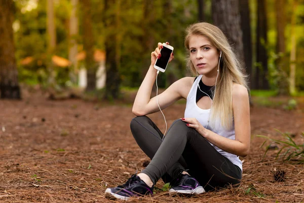 Pines ortasında güzel sarışın model cep telefonu ile kulaklık kullanarak oturma. Müzik