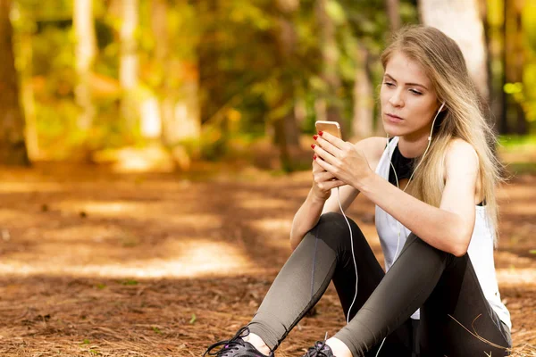 Pines ortasında güzel sarışın model cep telefonu ile kulaklık kullanarak oturma. Müzik