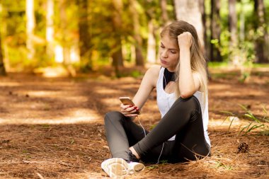 Pines ortasında güzel sarışın model cep telefonu ile kulaklık kullanarak oturma. Müzik