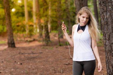 Güzel sarışın model cep telefonu ile kulaklık kullanarak ormandaki. Müzik