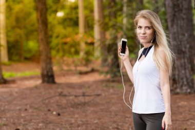 Güzel sarışın model cep telefonu ile kulaklık kullanarak ormandaki. Müzik