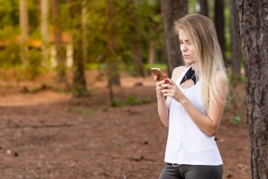 Güzel sarışın model cep telefonu ile kulaklık kullanarak ormandaki. Müzik