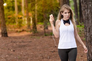 Güzel sarışın model cep telefonu ile kulaklık kullanarak ormandaki. Müzik