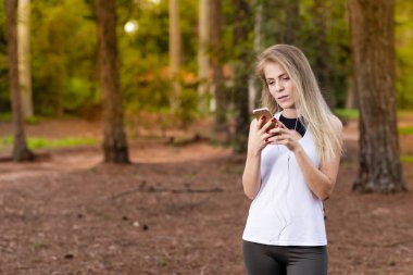 Güzel sarışın model cep telefonu ile kulaklık kullanarak ormandaki. Müzik