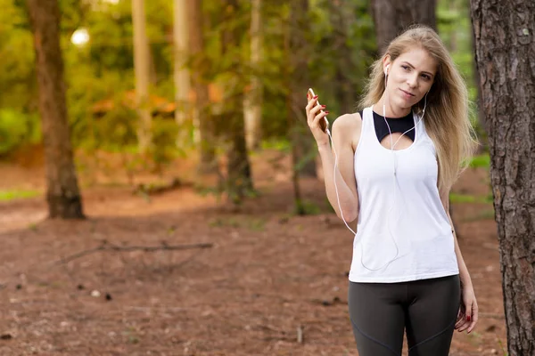 Beautiful blond model in forest using cellphone with headset. Listening to music