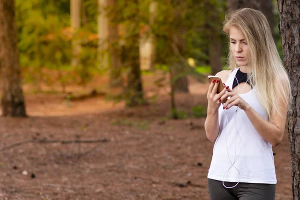 Beautiful blond model in forest using cellphone with headset. Listening to music