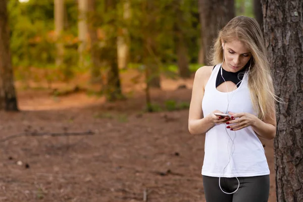 Beautiful blond model in forest using cellphone with headset. Listening to music