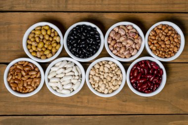 Fasulye kahverengi ahşap zemin üzerinde beyaz pot içinde sekiz çeşitleri.