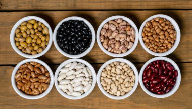 Fasulye kahverengi ahşap zemin üzerinde beyaz pot içinde sekiz çeşitleri.