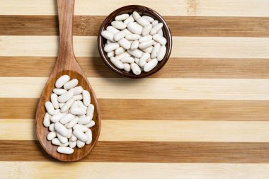 Pot ve tahta kaşık bambu ahşap arka plan üzerinde beyaz fasulye.