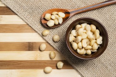 Macadamia fıstığı kahverengi seramik ve tahta kaşık bambu ahşap arka plan üzerinde.