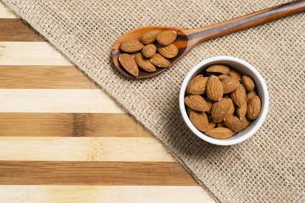 Natural almond within brown pottery and wooden spoon on bamboo wood background