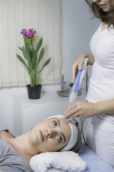 High frequency machine in spa salon. Young blond woman receiving electric darsonval facial massage after procedure at beauty room. Removal of acne from surface of face. Removing wrinkles.