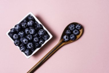 Pembe arka plan ve tahta kaşık üzerinde pot içinde Taze yaban mersini